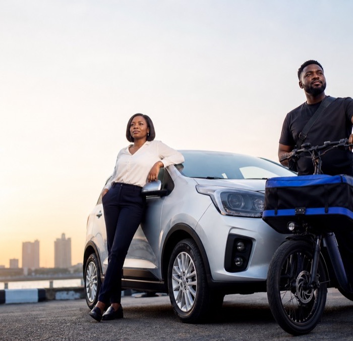 A CitiGo driver and a cargo-bike courier standing together at dusk, city skyline behind them